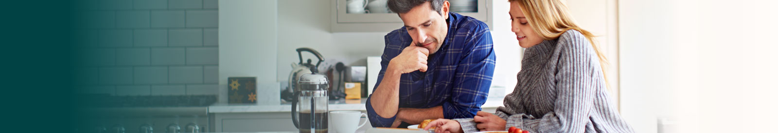 A couple standing at a kitchen bench looking looking at something together 