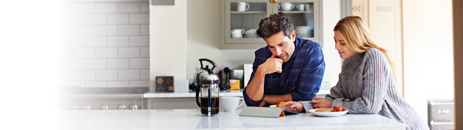 A couple in their kitchen looking at an iPad with a coffee plunger next to them