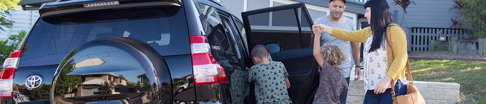 Young family getting in to car in front of house