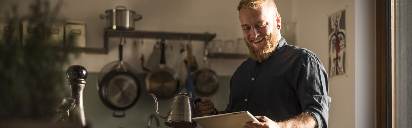 A bearded man with a fancy coffee pot in a kitchen