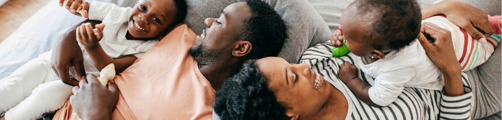 Man woman and two babies on a bed smiling