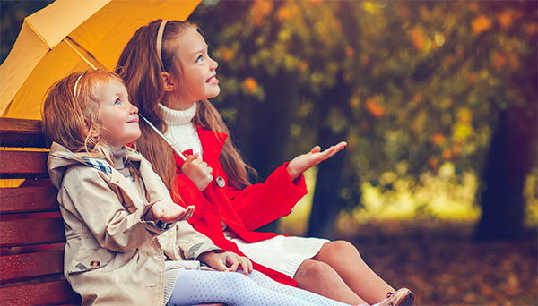 Girls sitting on park bench with an orange umbrella 